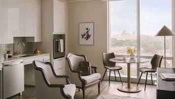 Una cocina moderna con armarios blancos, un comedor con mesa y sillas redondas, y un ventanal con vistas a la ciudad.