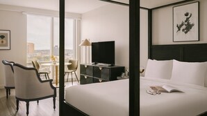 Habitación de hotel con cama, televisión, escritorio con lámpara, una silla y vistas a la ciudad.