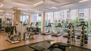 Une salle de sport équipée de divers appareils d’exercice, dotée de grandes fenêtres et offrant une vue sur un immeuble.