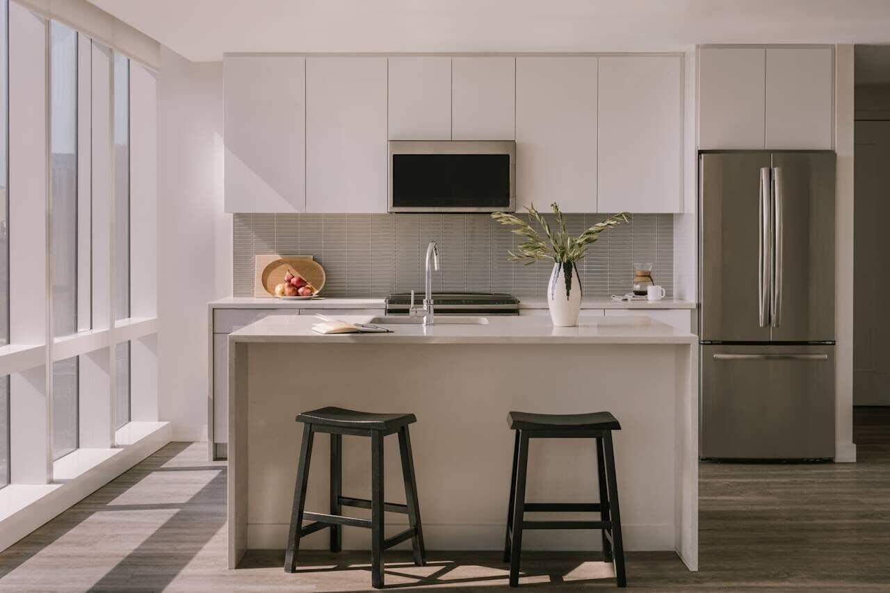 A modern kitchen with a central island, stainless steel appliances, and a large window.