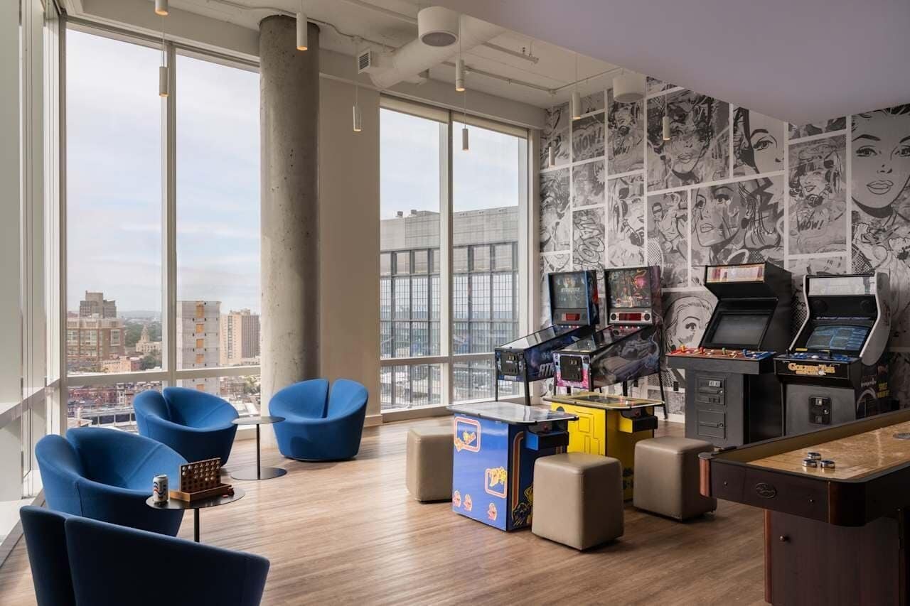 A room with large windows, arcade games, blue chairs, and a view of the city.