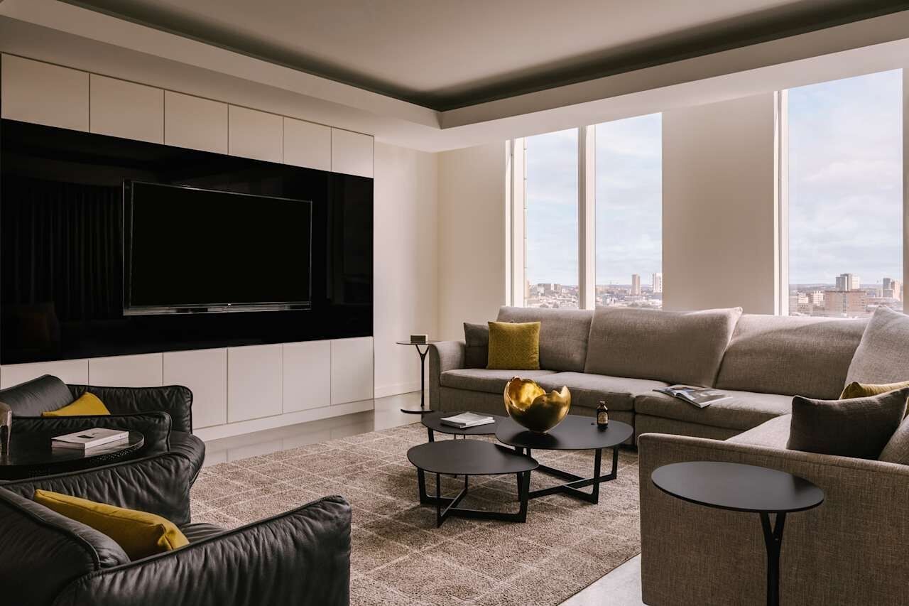 Una sala de estar moderna con un televisor de pantalla plana grande, un sofá, una mesa de centro y vistas de la ciudad a través de amplios ventanales.