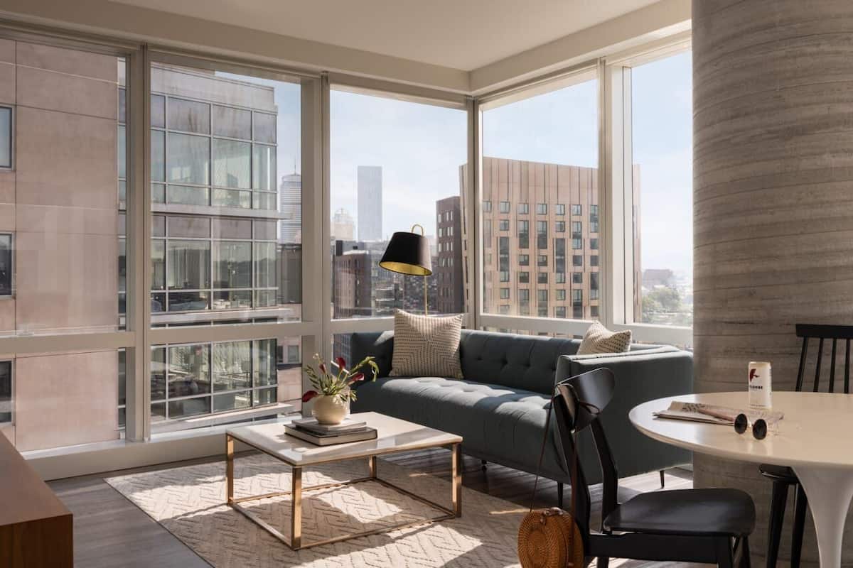 A modern living room with large windows, a sofa, a coffee table, and a lamp.