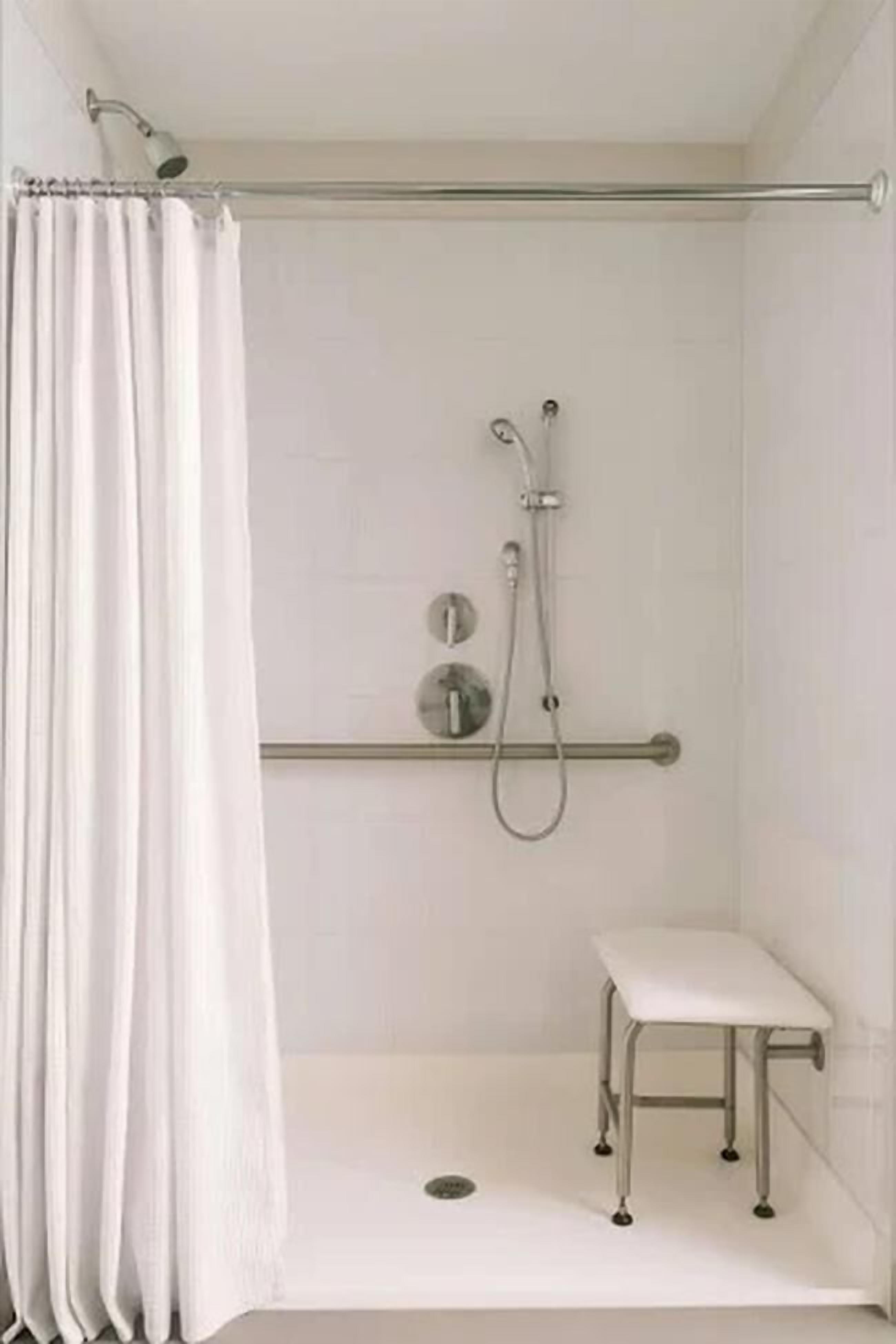 A shower area with a white curtain, a handheld showerhead, a handheld shower attachment, and a small white bench.