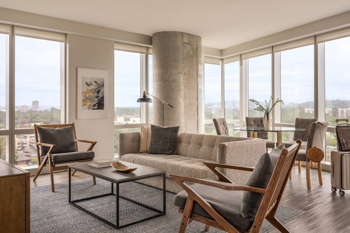 A modern living room with a large window, a sofa, a coffee table, and a chair.