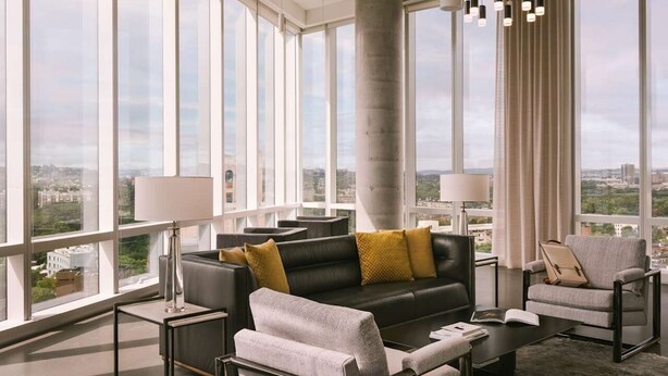 Una sala moderna con un sofá de cuero negro, sillones grises, una mesa de centro y un ventanal con vistas a la ciudad.