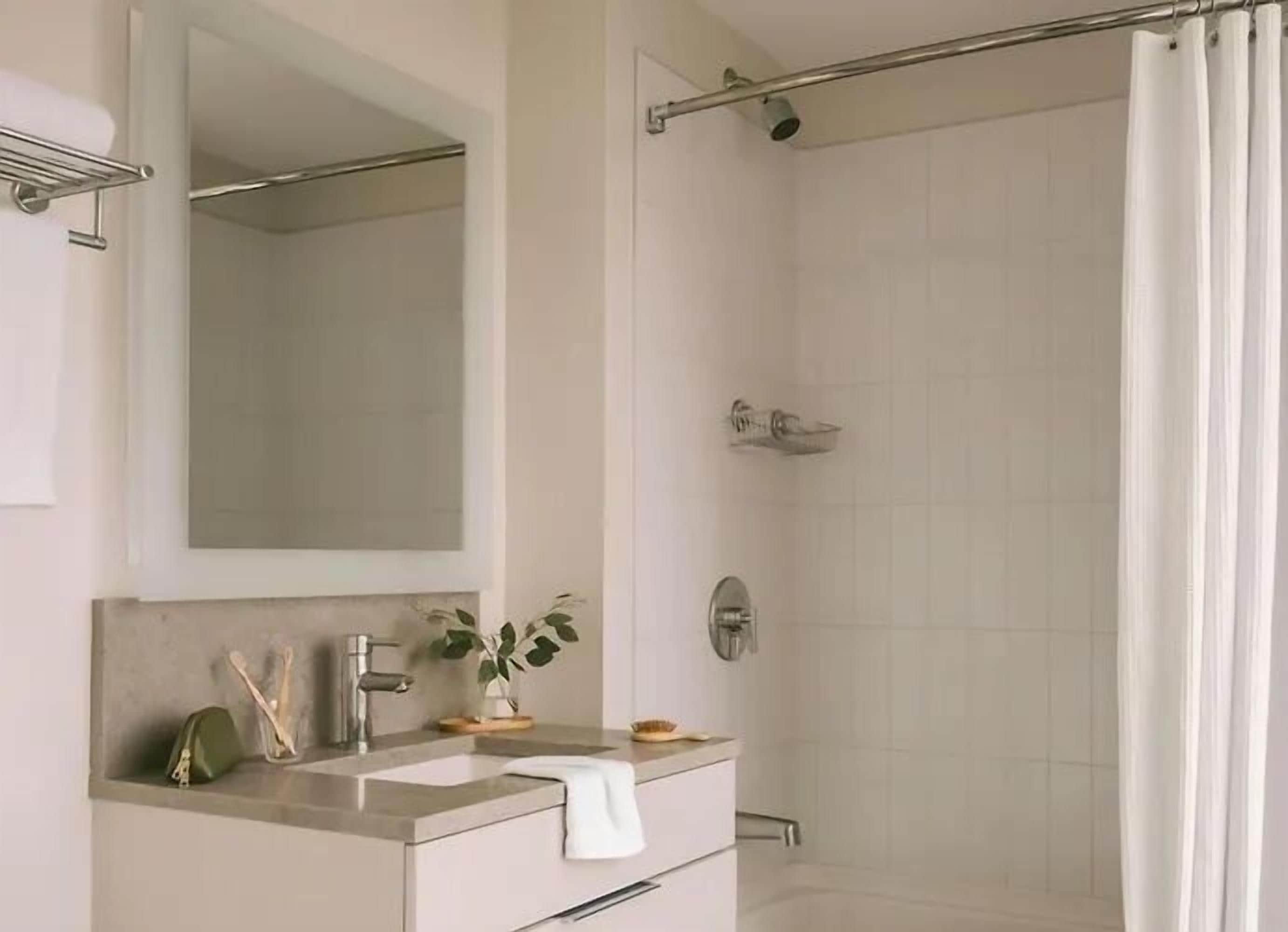A bathroom with a shower, a sink, a mirror, and a towel rack.