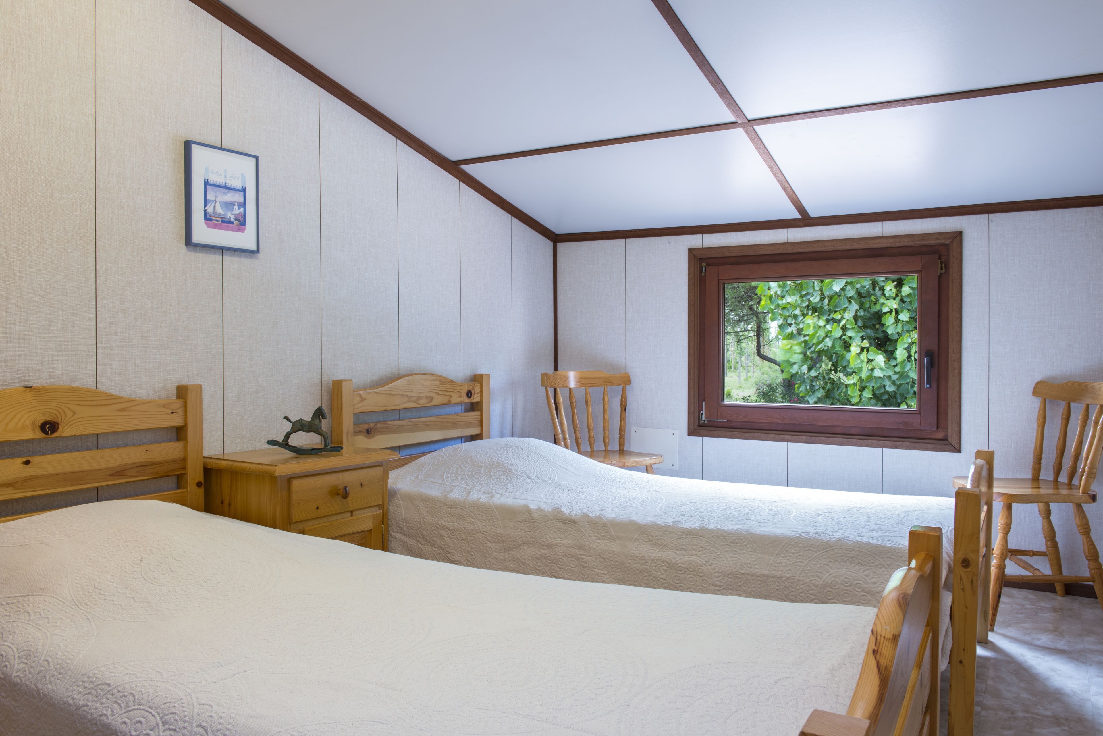 Un dormitorio con dos camas de madera, una ventana que da a zonas verdes y un cuadro en la pared.