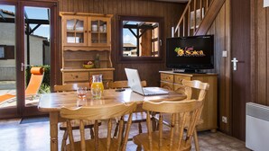 Une table à manger en bois, des chaises, un ordinateur portable, un téléviseur et un meuble avec des portes en verre.