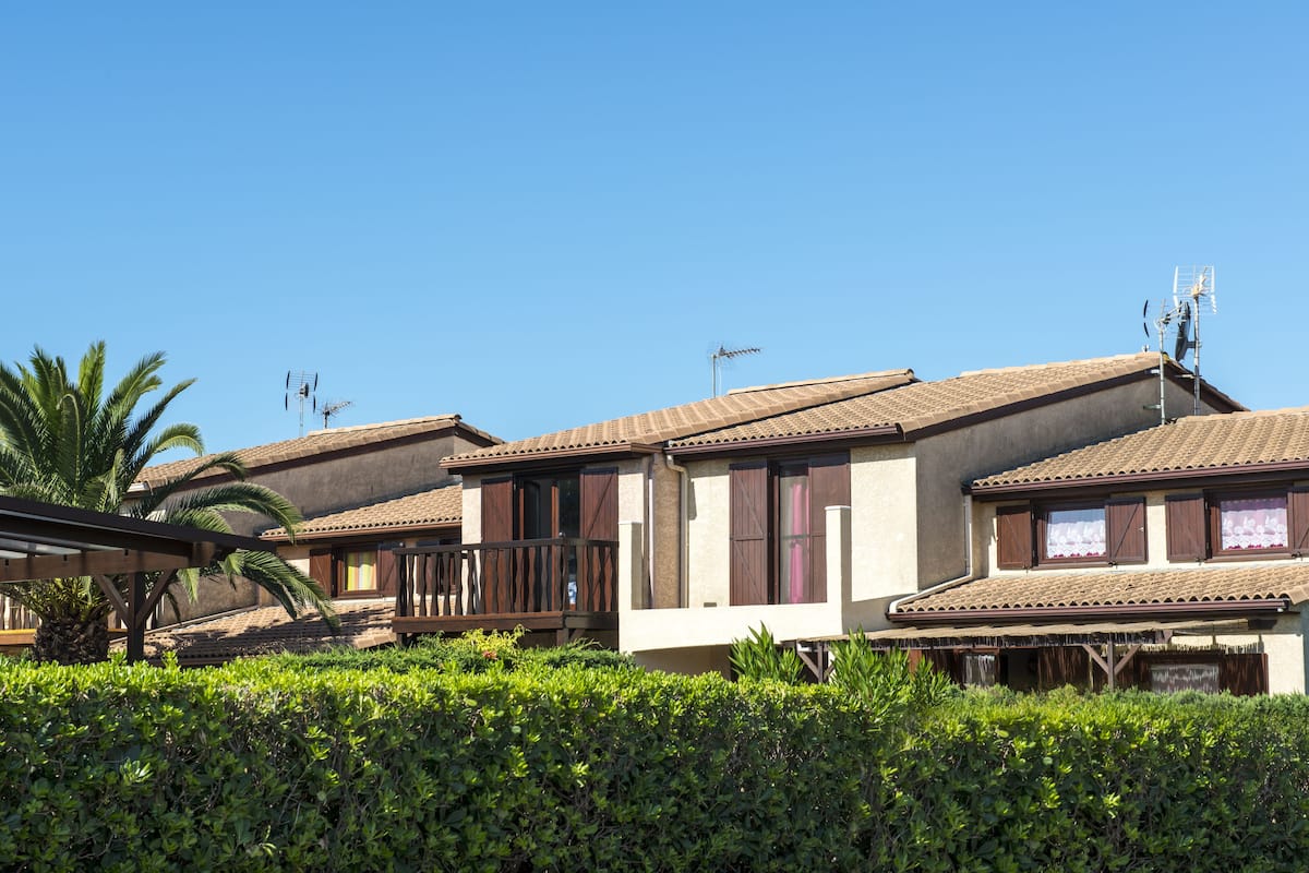 Une rangée de villas aux toits de tuiles, aux balcons en bois, sous un ciel d’un bleu limpide.