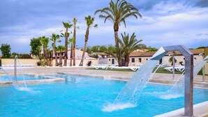 Ein Schwimmbecken mit Wasserspielen, Palmen und Gebäuden im Hintergrund.