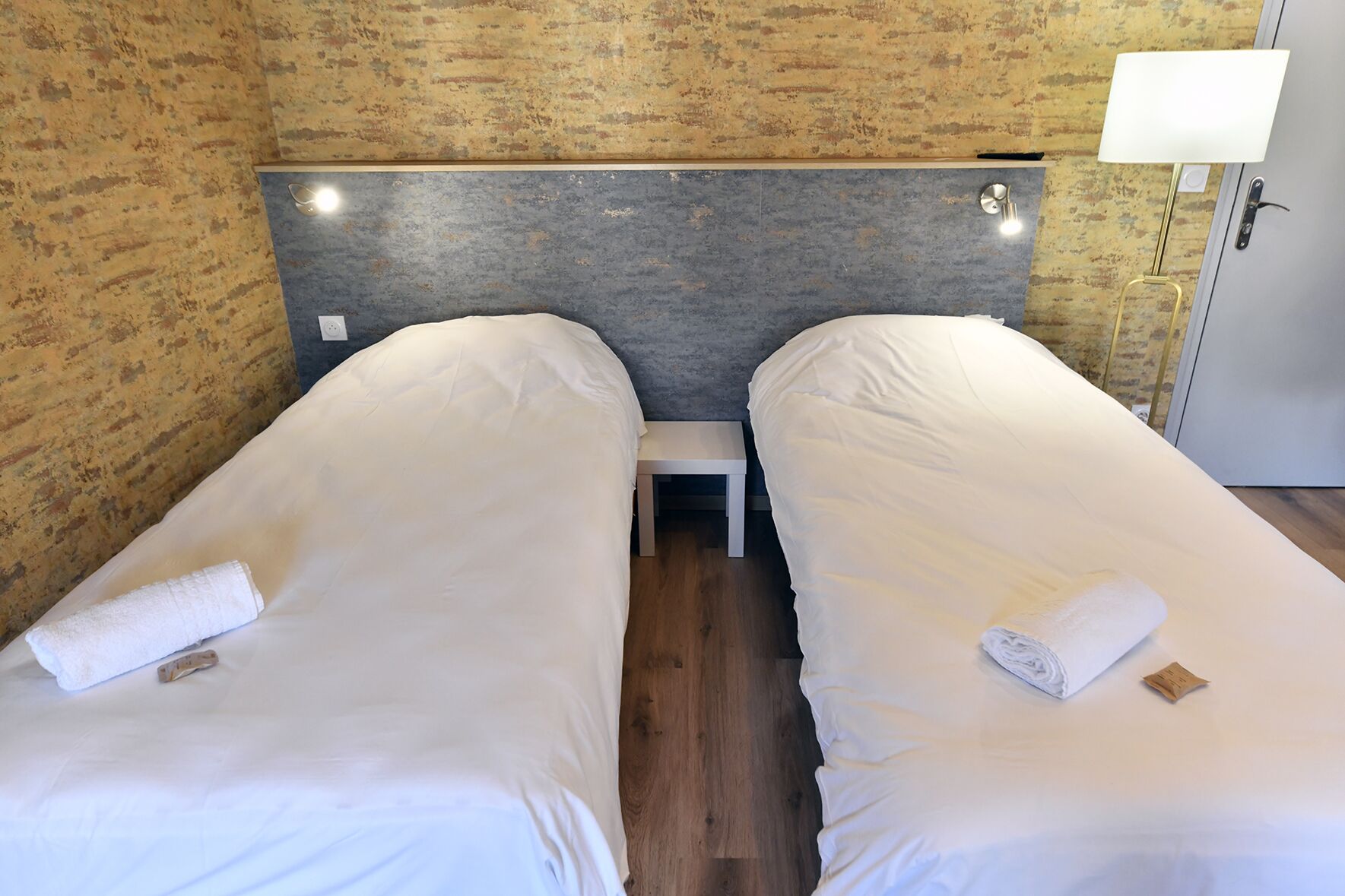 Een tweepersoonskamer met twee bedden, een klein nachtkastje en een lamp.
