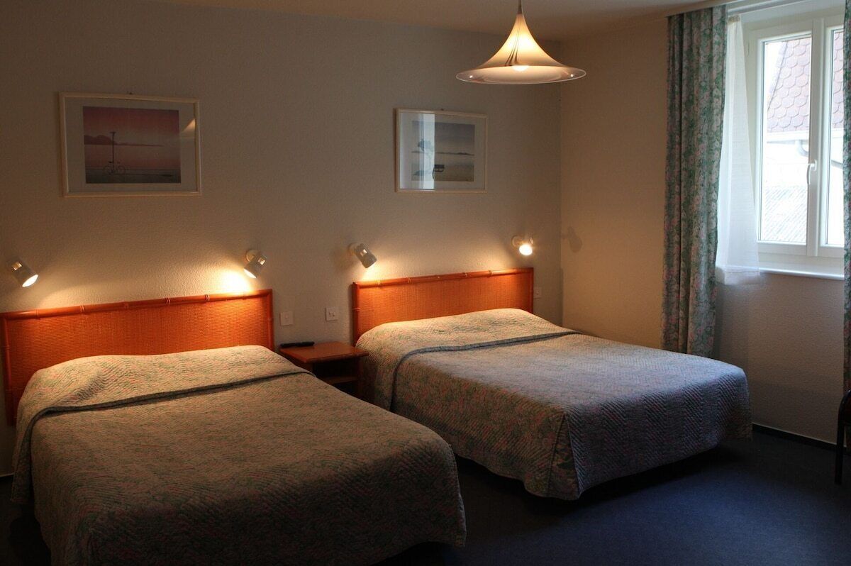 A hotel room with two single beds, a wooden headboard, a hanging light fixture, and two framed pictures on the wall.