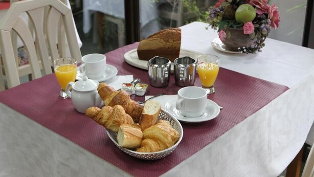 A breakfast table with croissants, orange juice, and a bowl of fruit. - Les Portes du Cantal (Massiac)