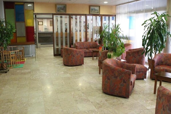 A lobby with patterned sofas, a reception desk, and potted plants. - Les Portes du Cantal (Massiac)