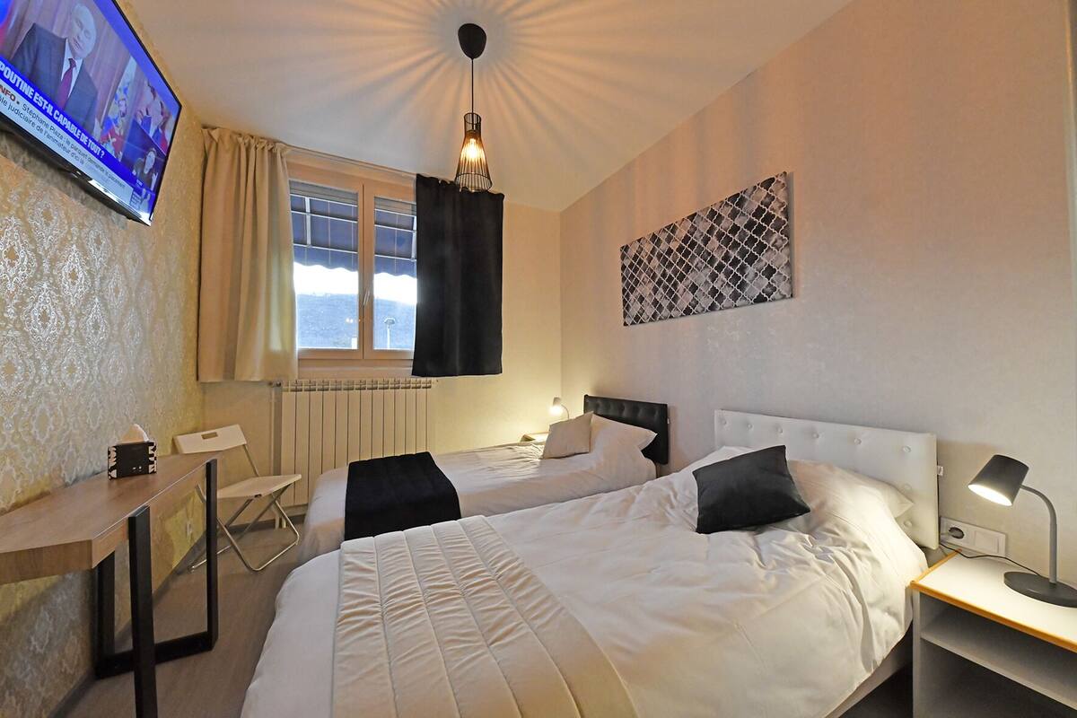Une chambre d’hôtel avec deux lits, un bureau, une chaise, une télévision et une fenêtre avec des rideaux.