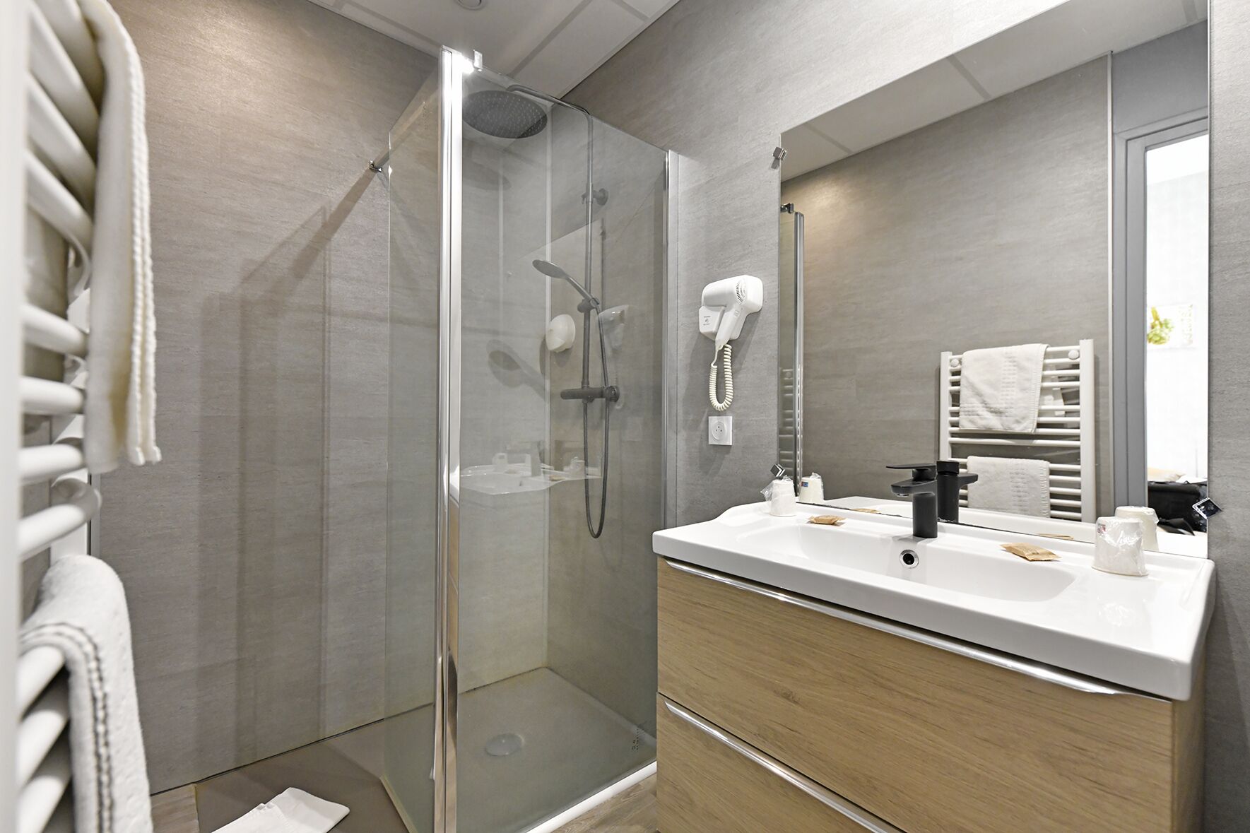 Een moderne badkamer met een douche in een glazen cabine, een wit wastafelmeubel en een kraan in zwart, en een grote spiegel.