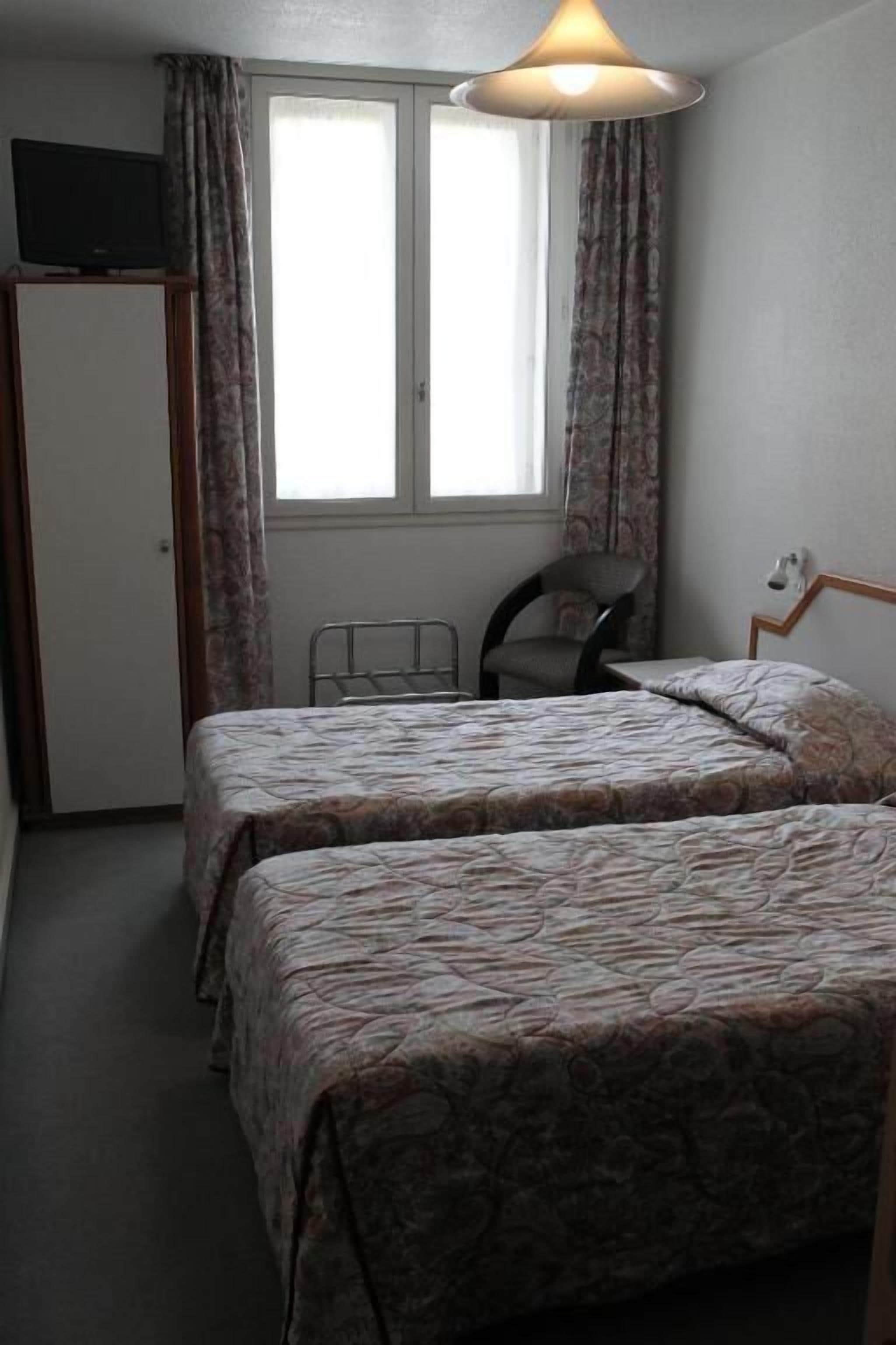 Un dormitorio con dos camas, una silla, un televisor sobre un mueble bajo y una ventana con cortinas.