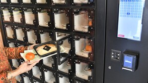 A person placing a tray with a pastry and an orange into a numbered locker. - Les Portes du Cantal (Massiac)