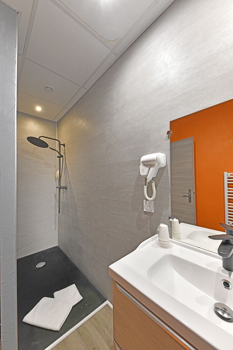 Une salle de bain moderne équipée d’une douche, d’un sèche-cheveux, d’un lavabo et d’un miroir.