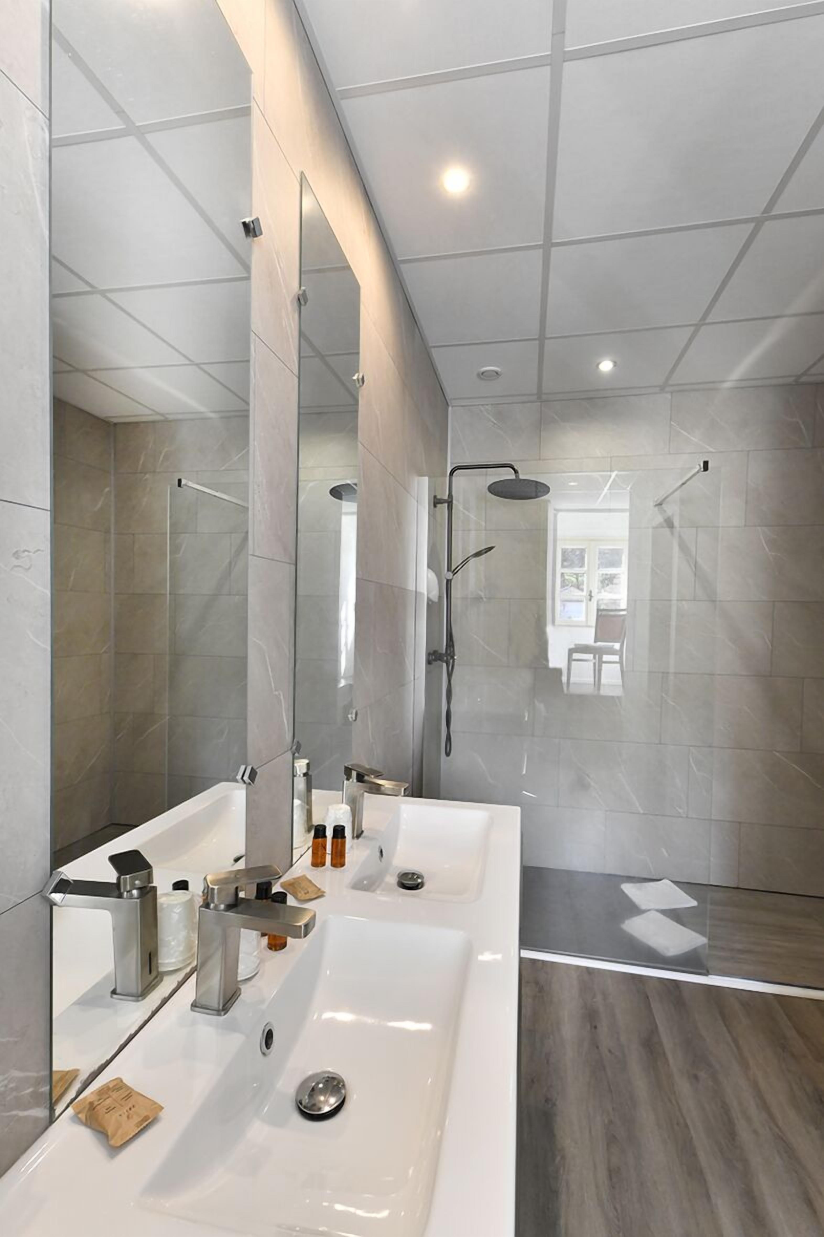 Un baño moderno con un espejo grande, dos lavamanos y una zona de ducha.