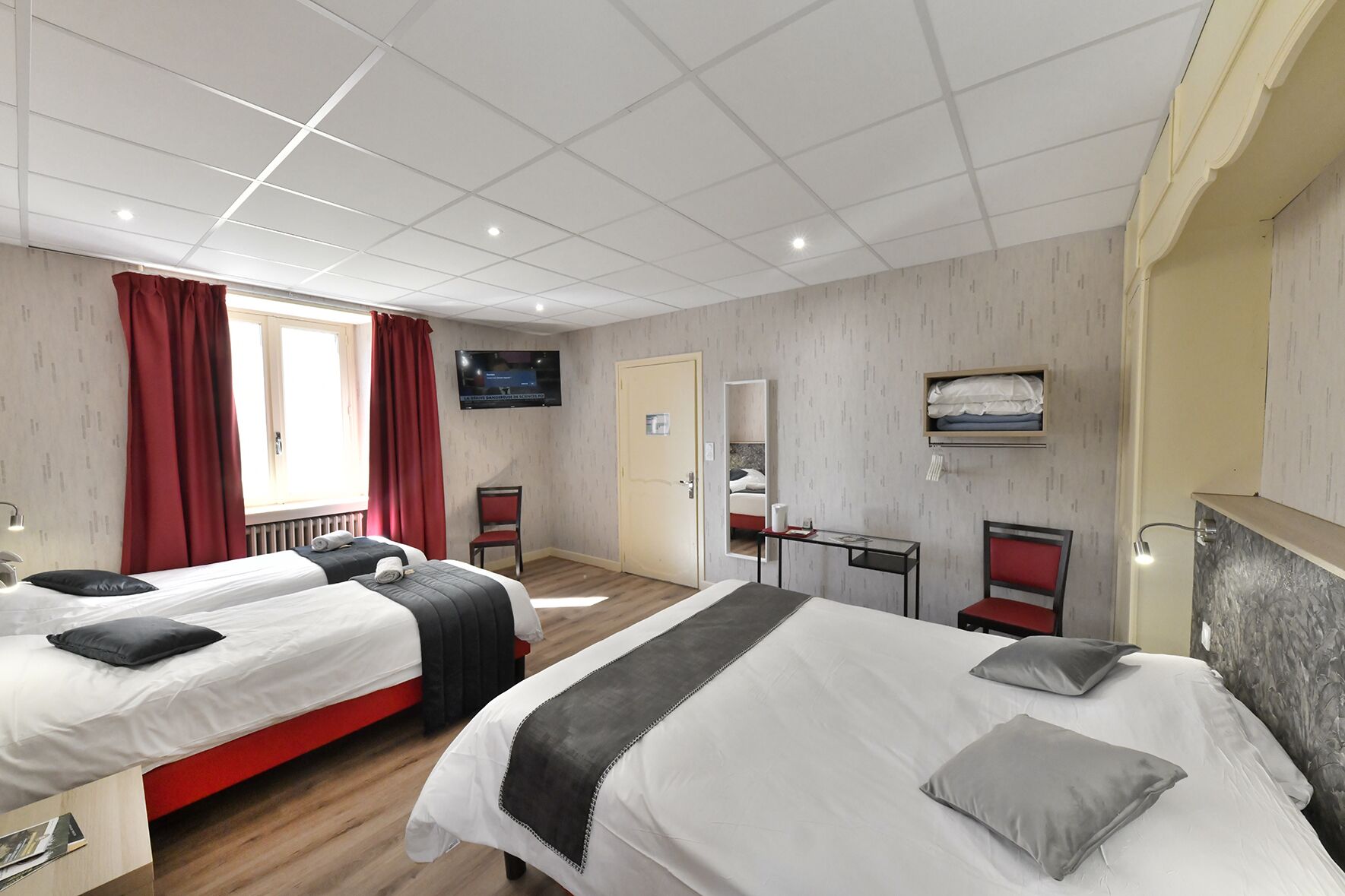 Ein Hotelzimmer mit zwei Betten, einem Fernseher, einem Spiegel, einem Schreibtisch und einem Kleiderschrank.