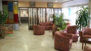 A lobby with patterned sofas, a reception desk, and potted plants. - Les Portes du Cantal (Massiac)