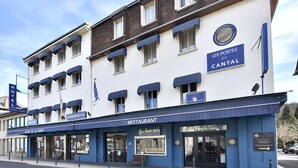 A hotel with a restaurant on the ground floor, multiple balconies, and a clear sky. - Les Portes du Cantal (Massiac)