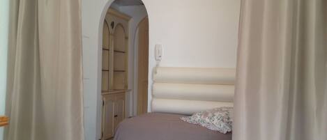Een slaapkamer met een bed, gordijnen, een telefoon en een deur naar een andere kamer.