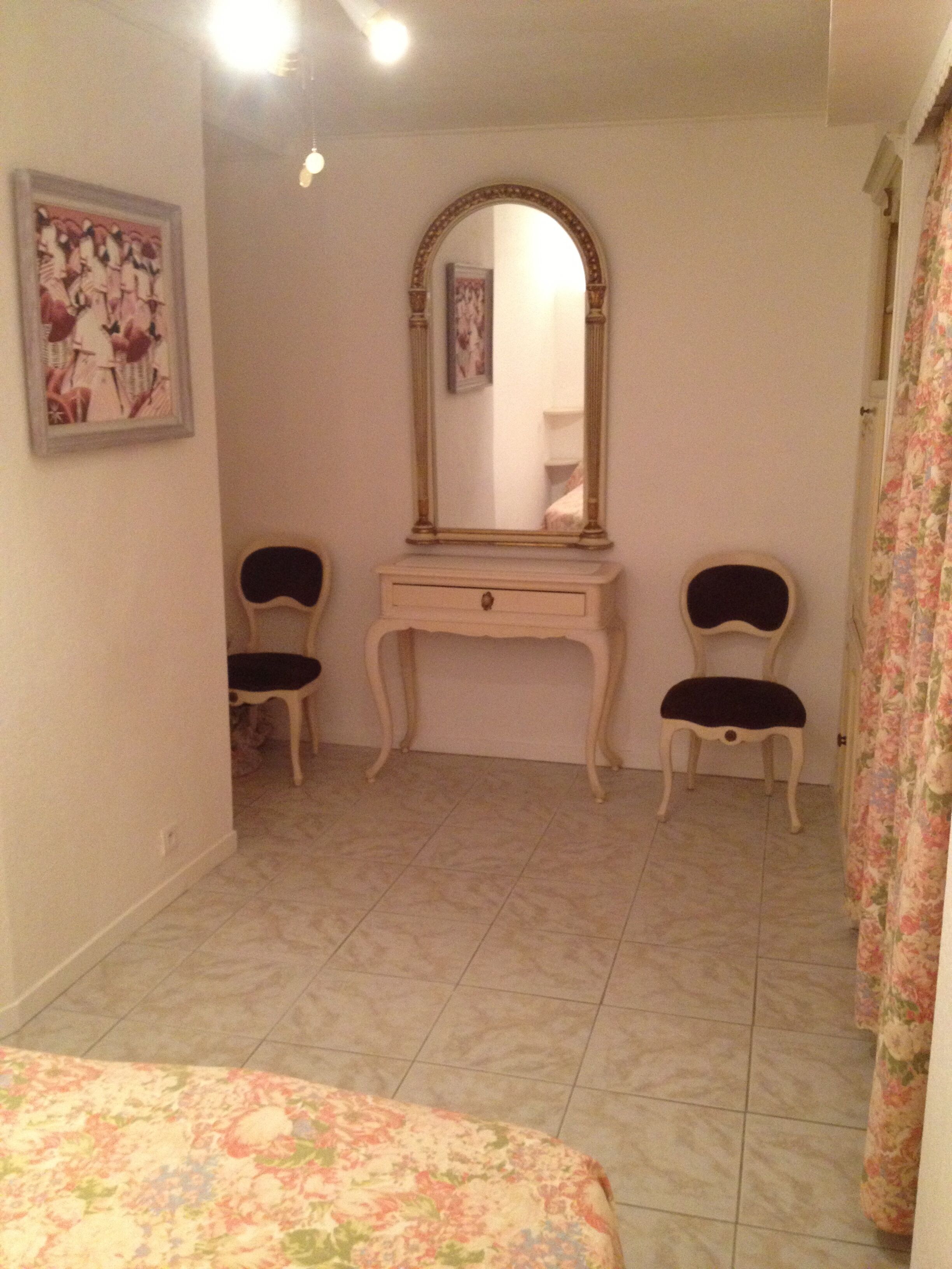 Un dormitorio con cama, cómoda con espejo, dos sillas y cortina con estampado floral.