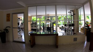 Uma academia com equipamentos de ginástica, uma janela grande e um vaso de planta.