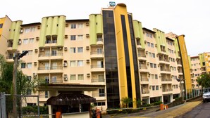Um hotel com vários andares, varandas, entrada central e área de estacionamento.