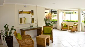 Um hall amplo com mobiliário de vime, balcão de recepção e uma grande janela com vista para o verde.