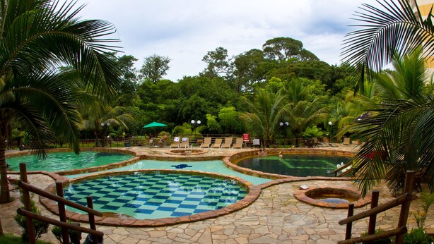 Uma área de piscina com várias piscinas, palmeiras e um caminho de pedra.
