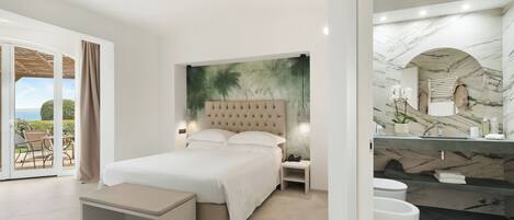 A modern bedroom with a large bed, a nightstand, a bench with slippers, a view of the outdoors, and a bathroom with a marble sink and tub.