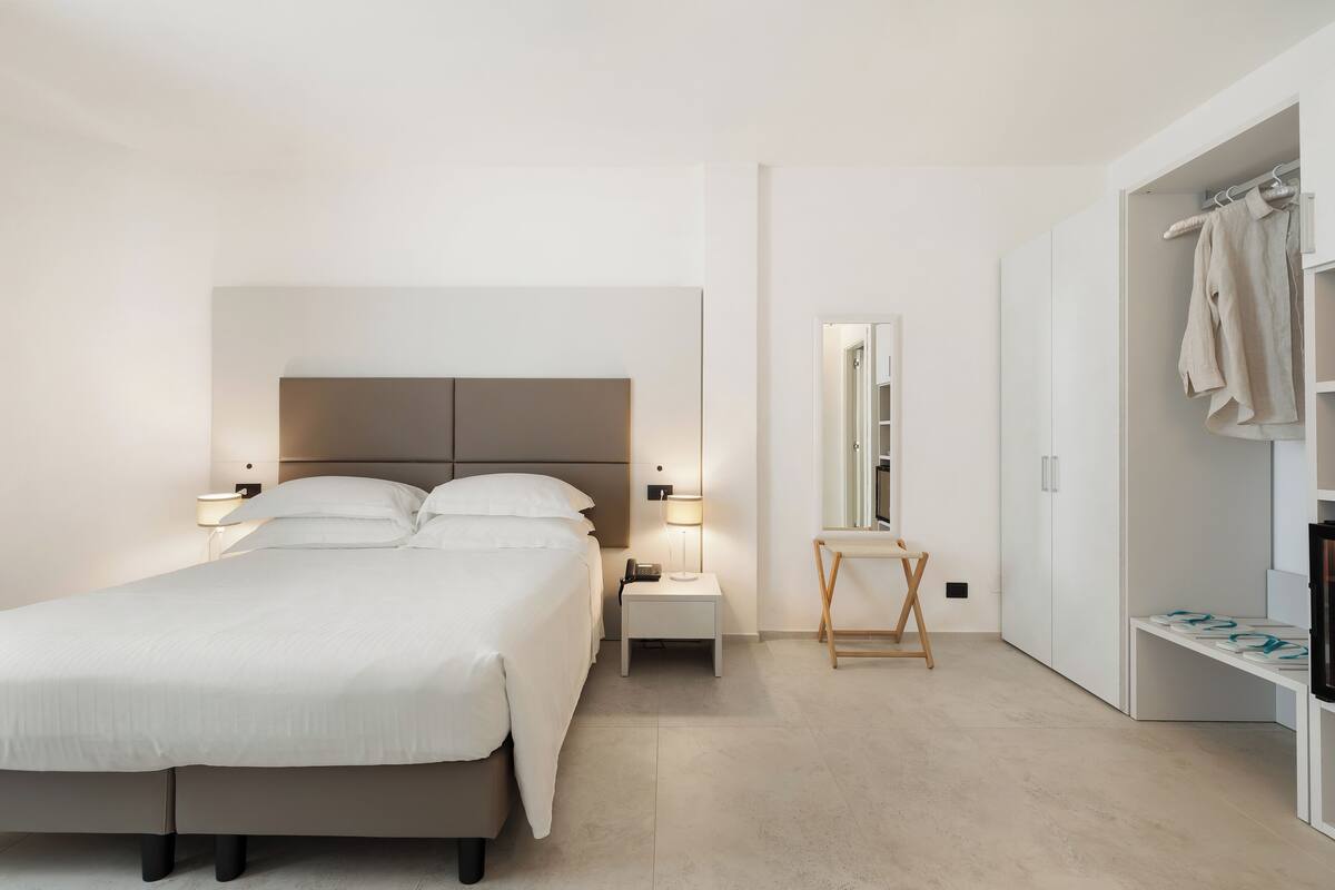 Ein modernes Hotelzimmer mit einem großen Bett, Nachttischen, einem Spiegel und einem Kleiderschrank.