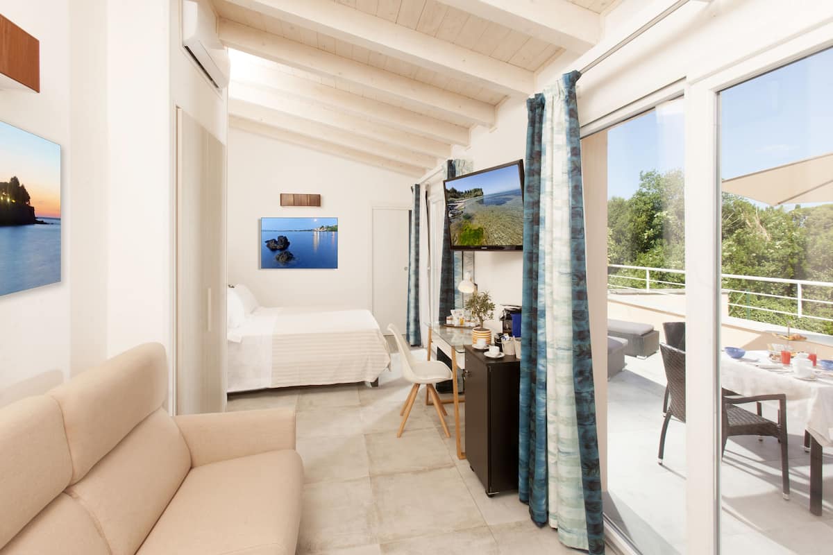 Ein Hotelzimmer mit einem Bett, einer Couch, einem Schreibtisch mit Computer sowie einem Balkon mit Tisch und Stühlen.
