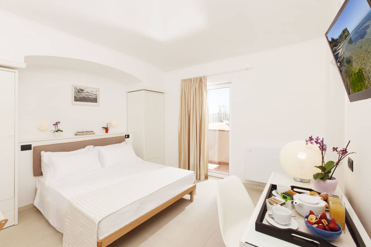 Ein Hotelzimmer mit Bett, Schreibtisch mit Frühstücksangeboten, einer Lampe und Blick ins Freie.