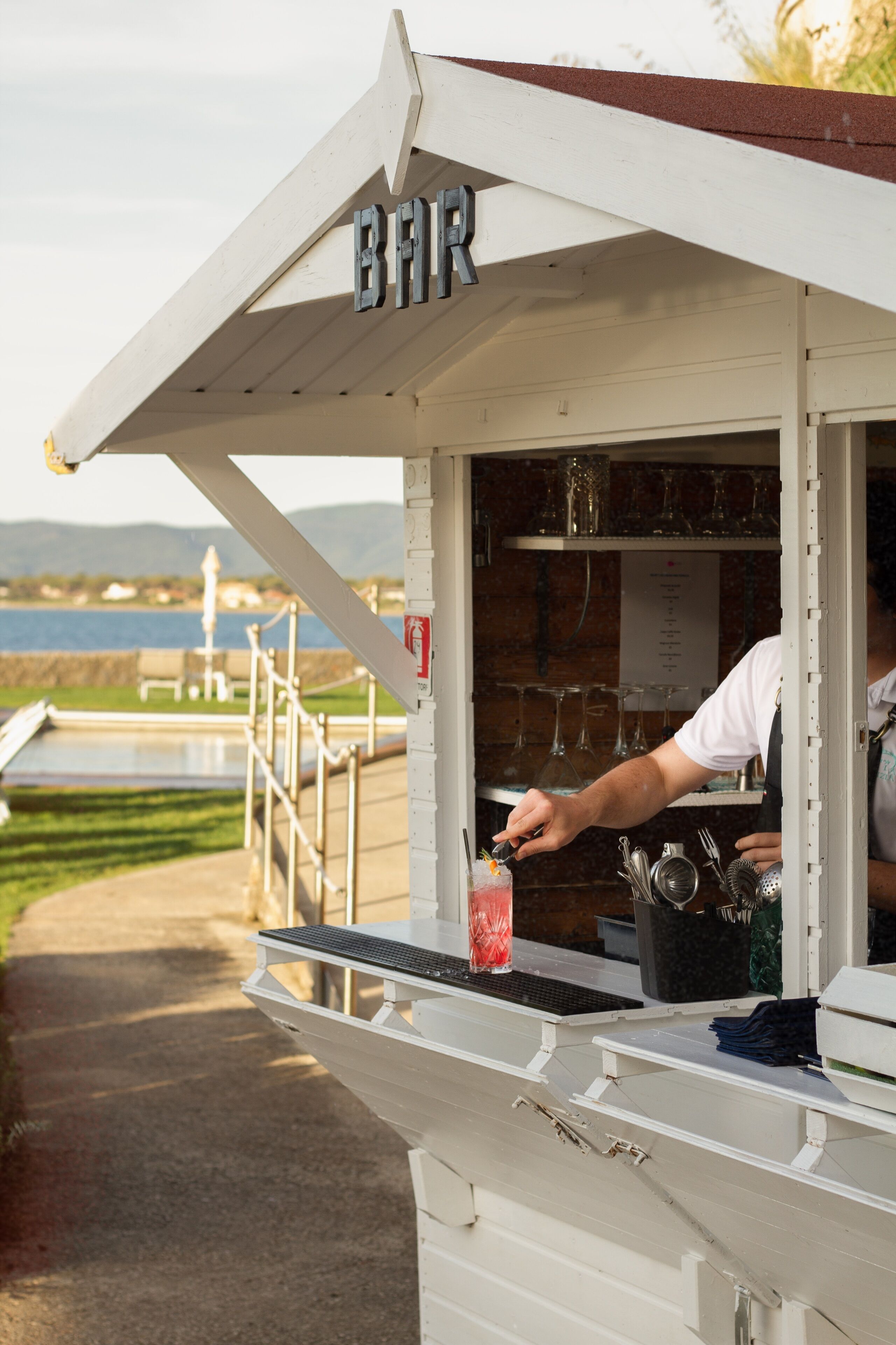 Un stand de vente de bières avec une enseigne, une personne préparant une boisson, et en arrière-plan, une étendue d’eau.