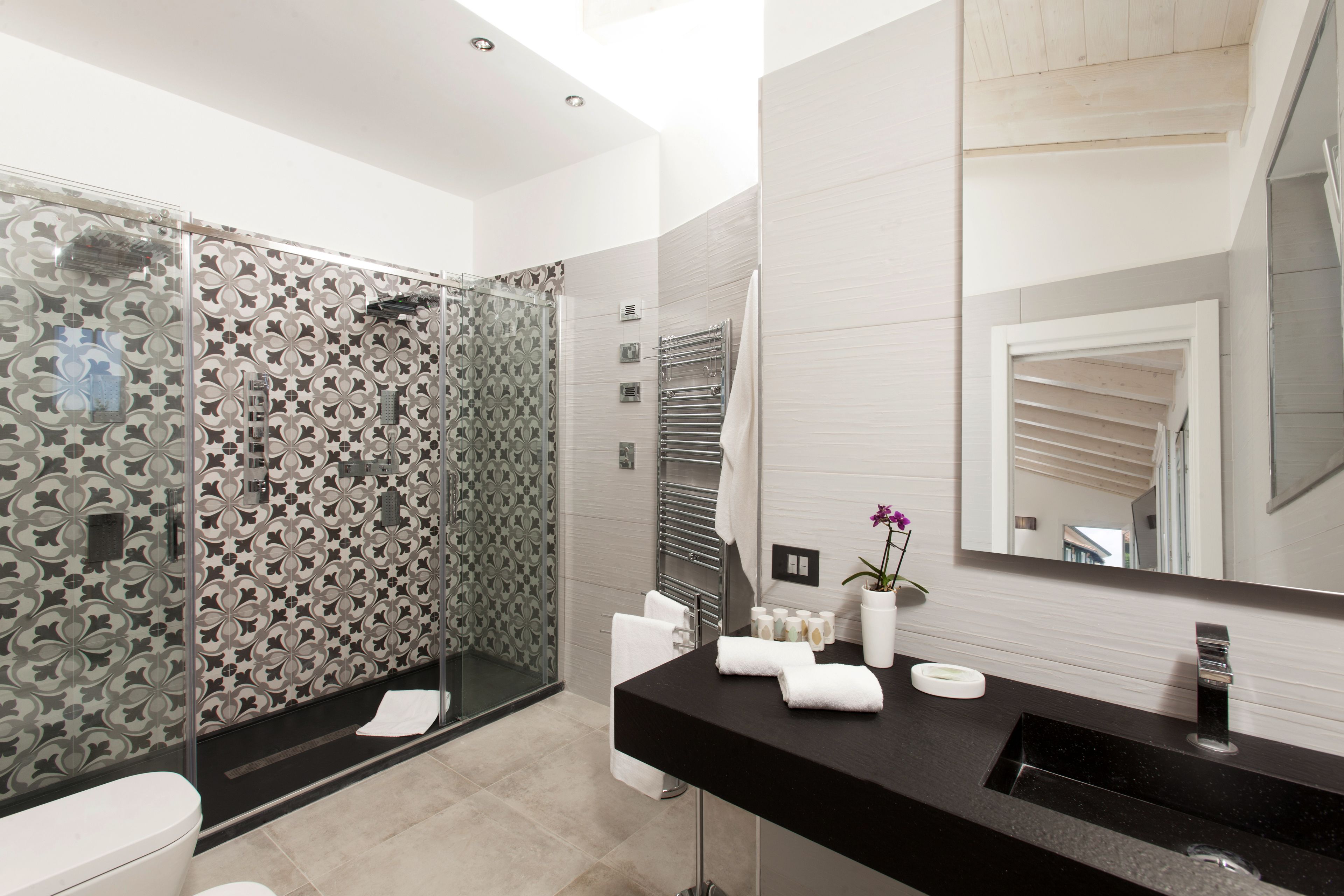 A modern bathroom with a glass shower enclosure, a black sink, and a large mirror.