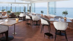 Un restaurant doté d’une terrasse offrant une vue sur la mer, avec un mobilier moderne et des plantes en pot.
