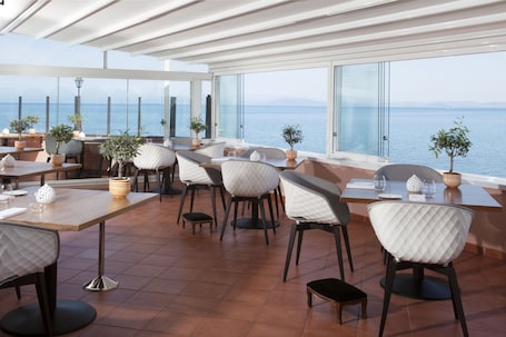 A restaurant with outdoor seating overlooking the sea, featuring modern furniture and potted plants.