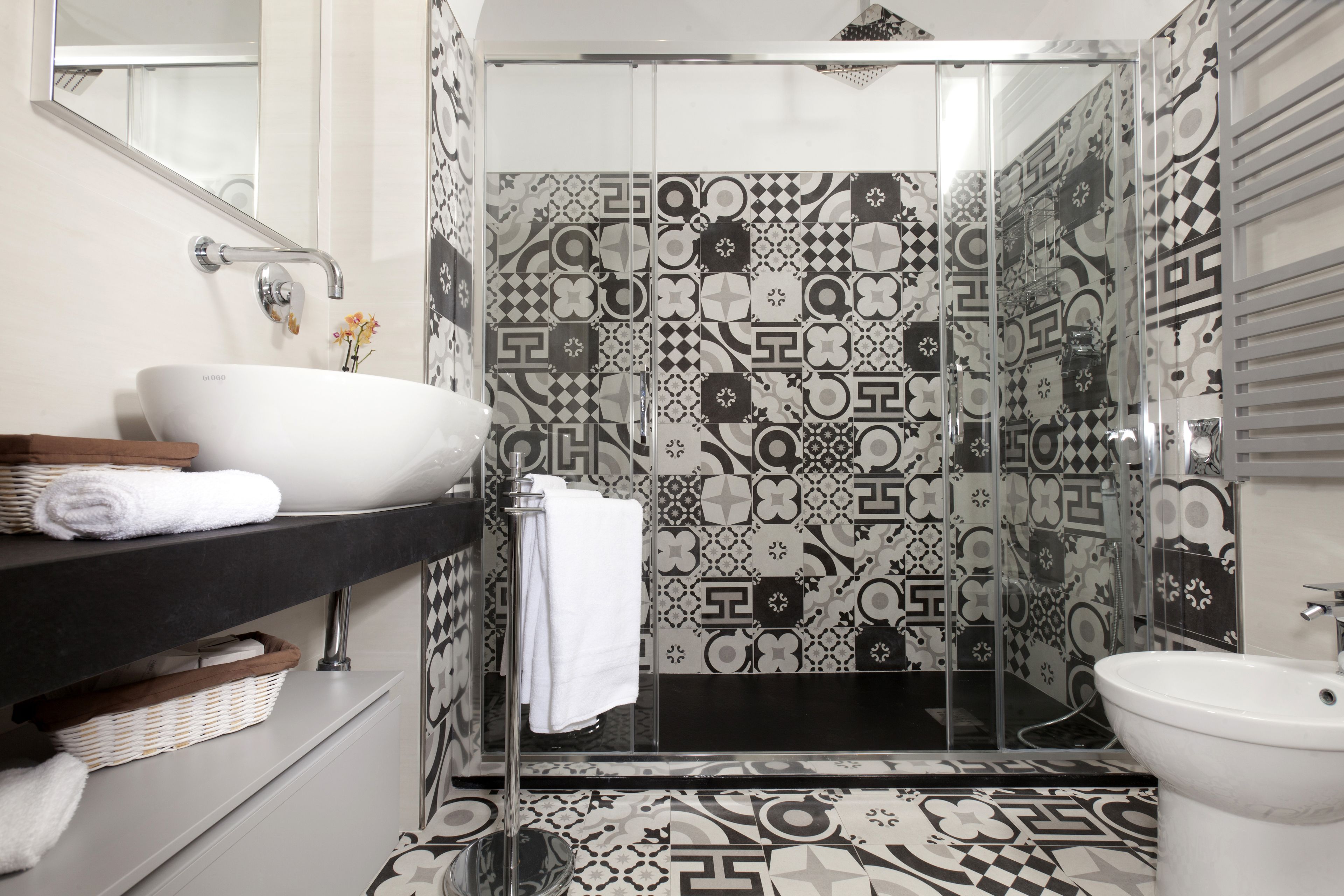 Un baño moderno con un lavabo blanco, encimera negra y baldosas estampadas.