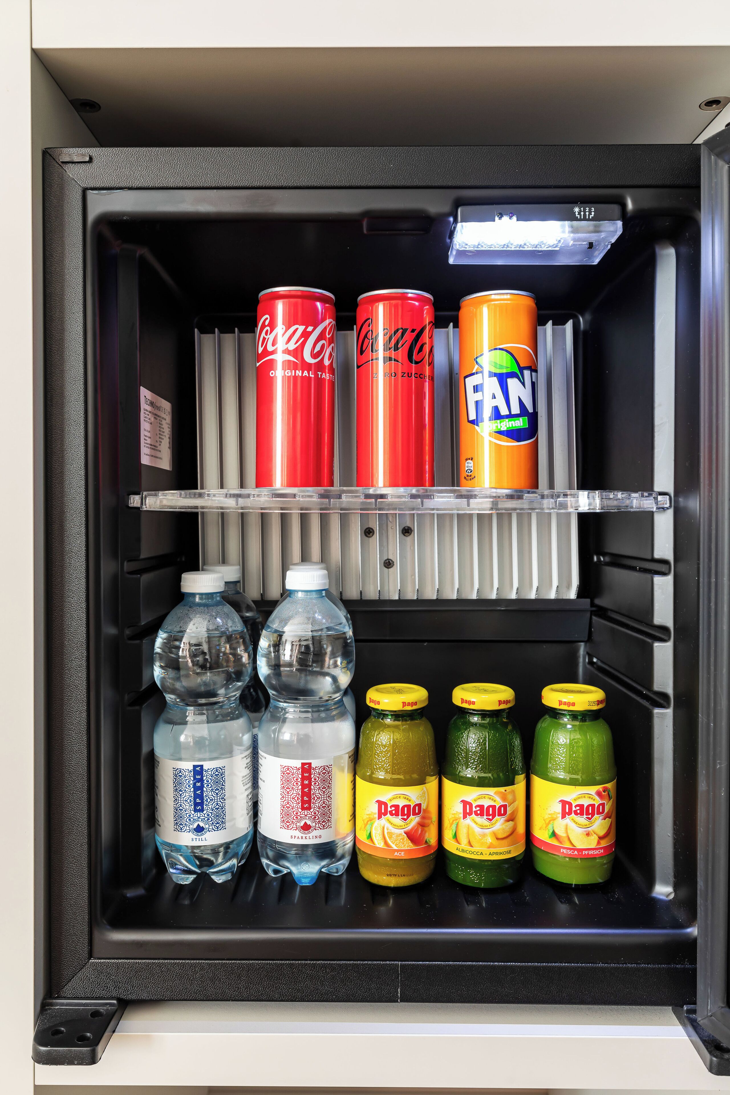 A refrigerator stocked with beverages including Coca-Cola, Fanta, and various water and juice options.