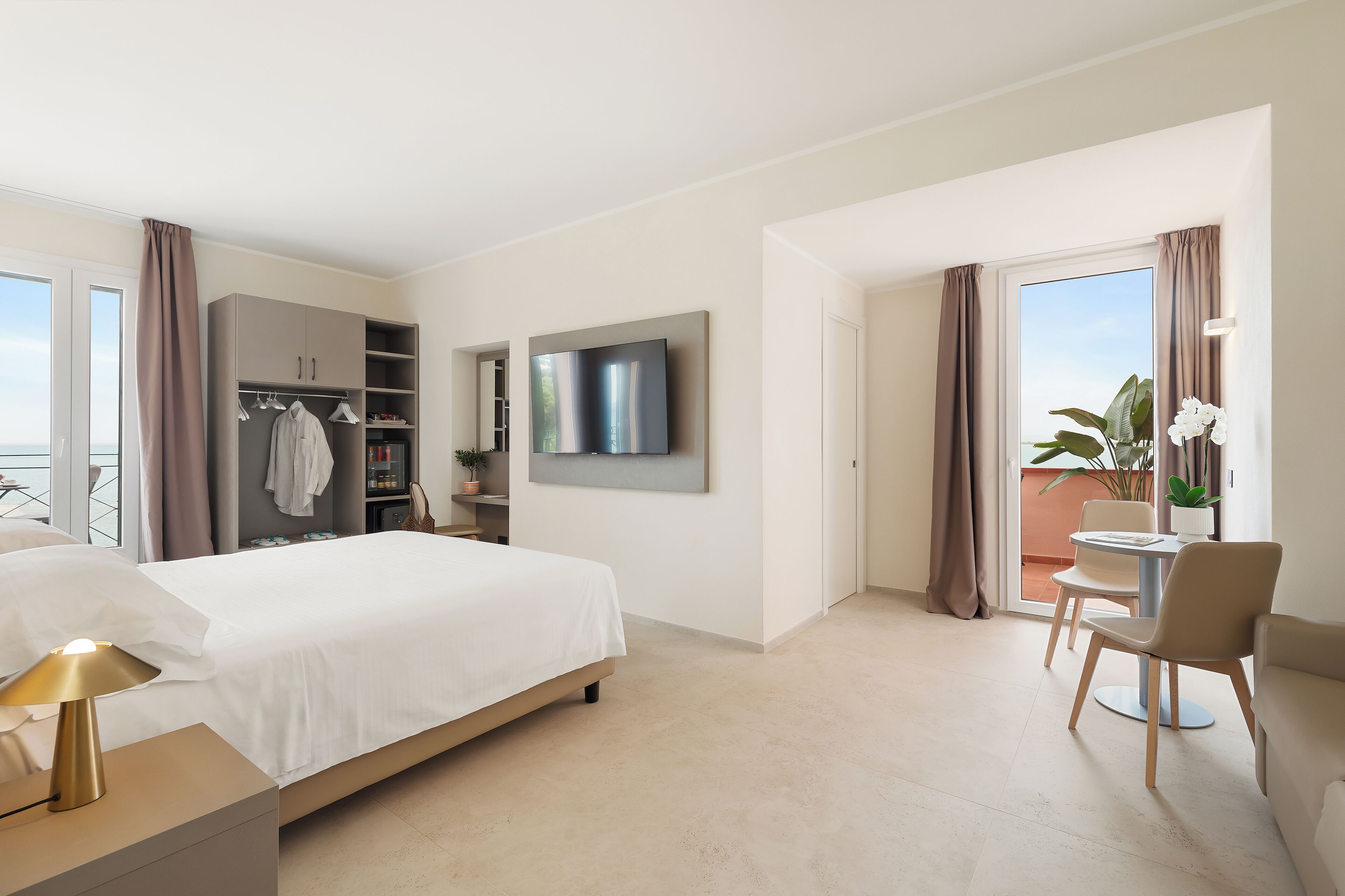 Una habitación de hotel moderna con una cama, un televisor, un balcón con una silla y un armario.