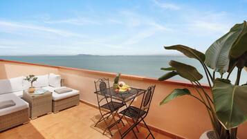 Un balcón con un sofá de mimbre, una mesa metálica con fruta y una planta grande.