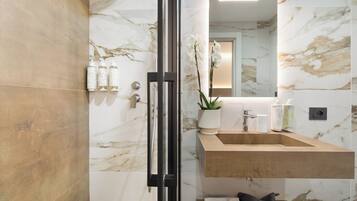 A modern bathroom with a marble backsplash, a glass shower enclosure, a wooden vanity, and a mirror above the sink.