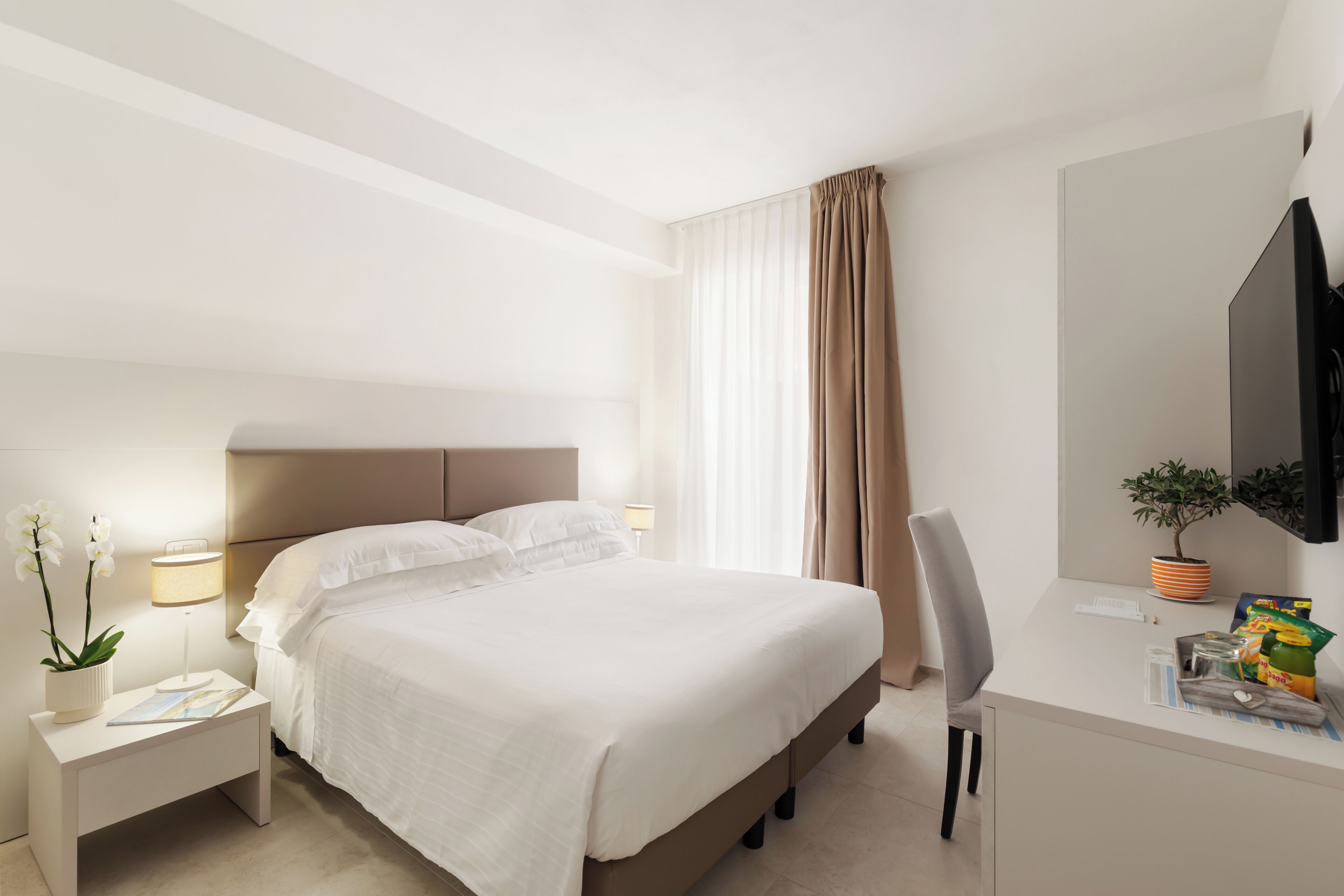 Una camera d'albergo con un letto, un comodino, una lampada e una scrivania con una sedia.