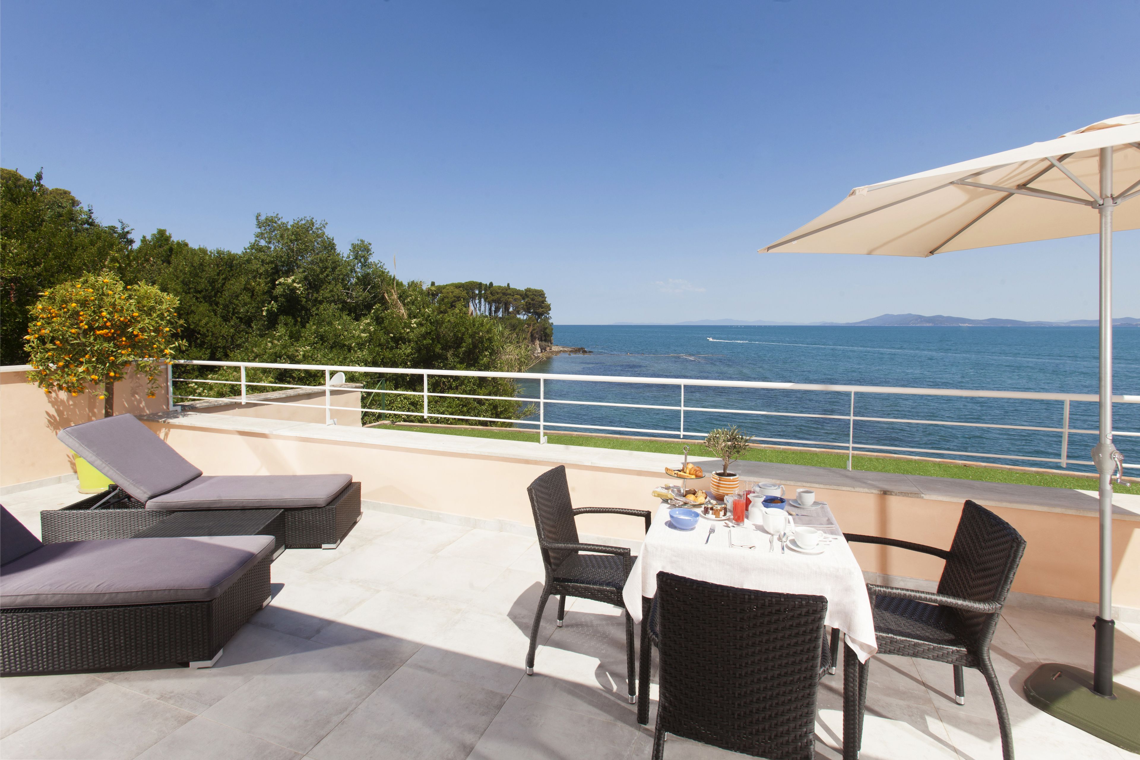 A terrace with wicker furniture, a table set for dining, and a view of the sea.