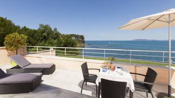 A terrace with wicker furniture, a table set for dining, and a view of the sea.